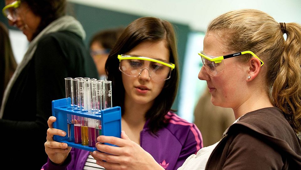Zwei Schülerinnen mit Schutzbrillen und einem Halter voller Reagenzgläser