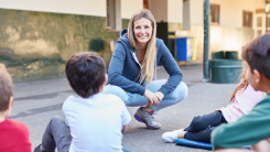 Eine Lehrperson/Trainerin hockt in einem Kreis von Kindern